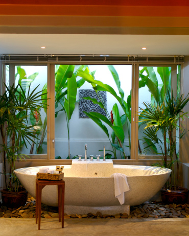 A tropical zen bathroom, a washroom with a wall of the tropics, free standing bath in this very natural setting.