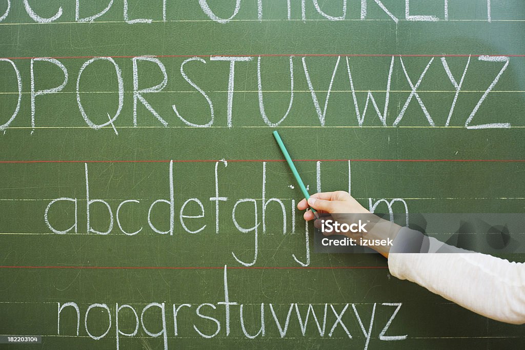 Teaching The Alphabet A teacher's arm pointing at the letters of the alphabet on a blackboard. Adult Stock Photo