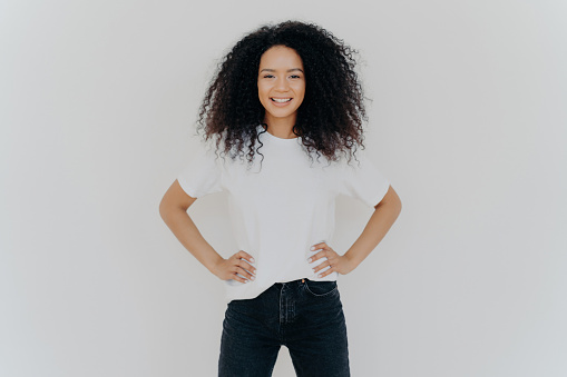 Confident Black woman with curly hair in white tee and jeans against a light background