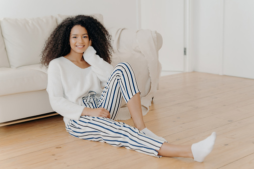 Relaxed Black woman with curly hair sitting on the floor, smiling, home interior