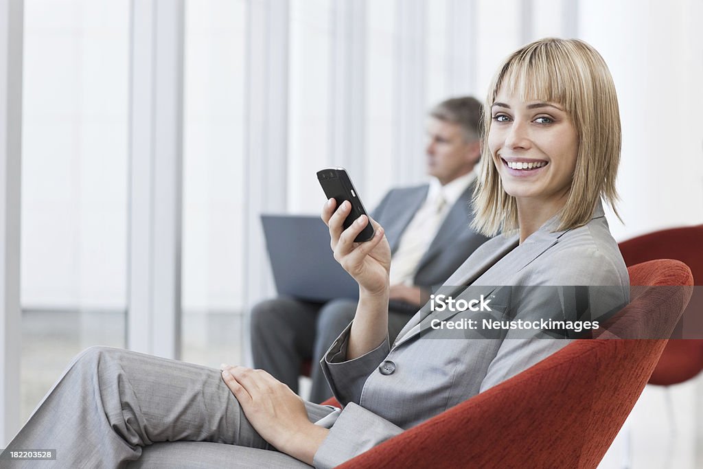 Feliz Mulher de negócios segurando um celular com os colegas no fundo - Foto de stock de Mensagem de Texto royalty-free