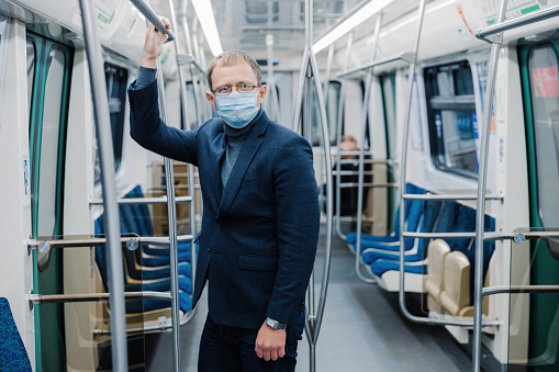 Businessman commuting on a subway train, holding onto a handle, wearing a face mask