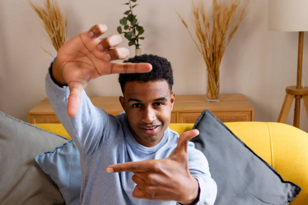 istock Young african american man making frame with hands while sitting on sofa at home 1822045944