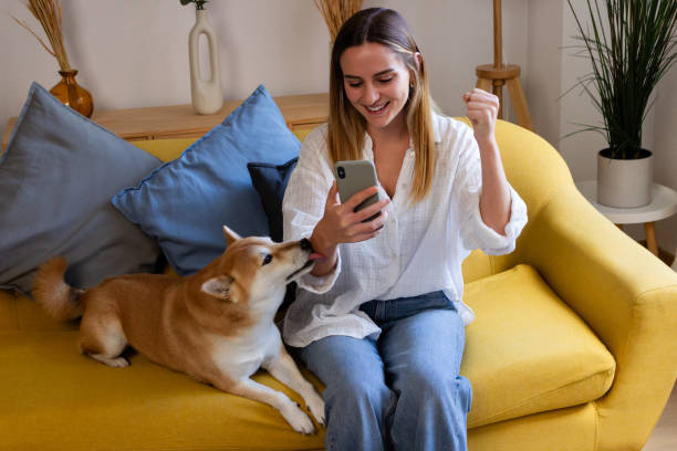 istock Smiling young woman sitting on sofa with her dog and using smartphone. 1822046499