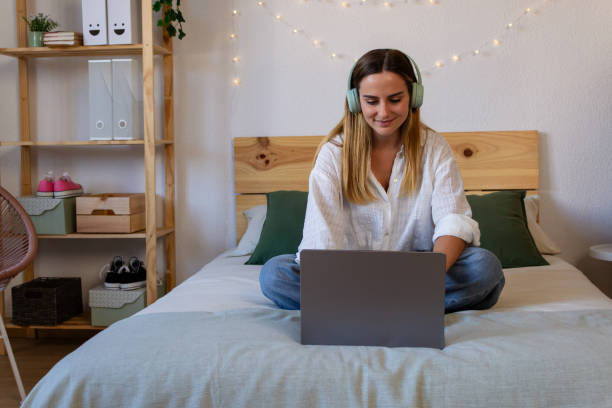 istock Happy young woman using laptop while sitting on bed in bedroom at home 1822051279