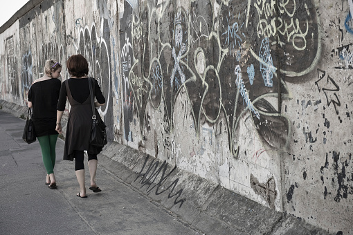 Two women walk along a remaining section of the Berlin wall in the former East Berlin by the river Spree.