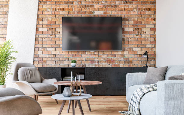 moderní obývací pokoj s televizí namontovanou na cihlové zdi, šedou pohovkou, židlemi a konferenčním stolkem a dekoracemi - knihovna police fotky - stock snímky, obrázky a fotky