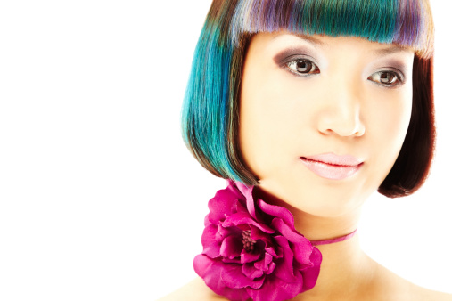 Young adult female model wearing a multi-colored wig and a flower around her neck. Horizontally framed shot.