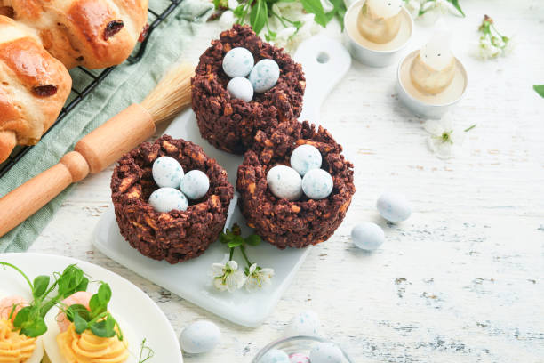 istock Easter brunch or breakfast. Easter chocolate nest cake with chocolate candy eggs, traditional hot cross buns and deviled eggs with bouquets of blooming apple trees. Spring Easter holiday food concept. 1822070195