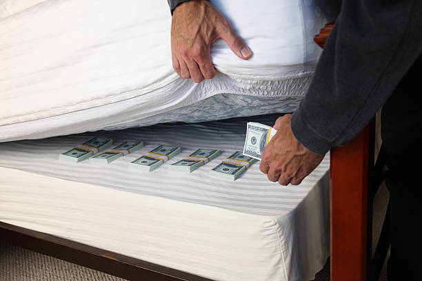 Hiding Money Under The Mattress Man hides a stack of bills under his mattress. gchutka stock pictures, royalty-free photos & images
