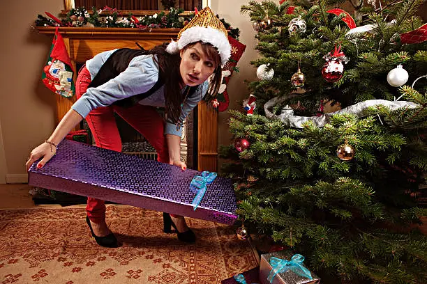 Girl trying to put a christmas present under the tree before anyone sees her