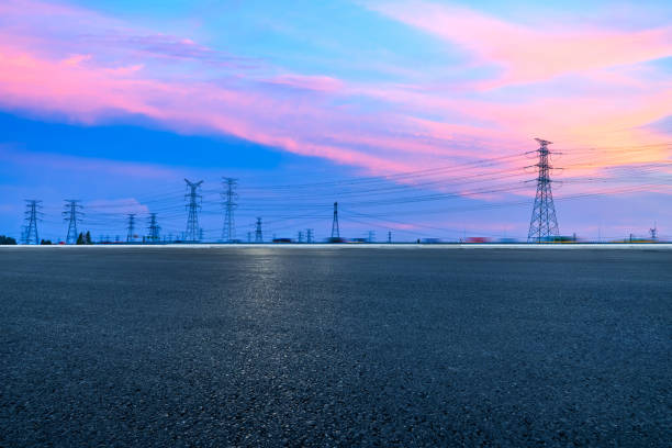 夕暮れ時のアスファルト道路と高圧送電塔の風景