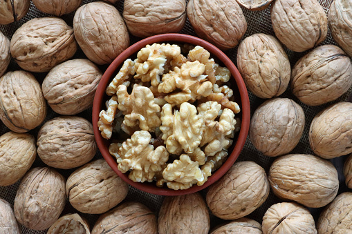 Stock photo showing close-up, elevated view of some walnuts that have been shelled and are piled high in a brown dish, surround by unshelled walnuts. Raw walnuts are considered to be a very healthy snack food, containing a wealth of essential Omega-3 fatty acids, antioxidants and protein, and boasting a list of health benefits while reducing stress.