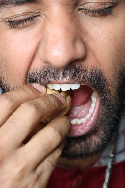 Full frame image of Indian man trying to crack walnut with teeth, foolish behaviour, eyes tight shut, gaping mouth, facial hair, focus on foreground stock photo