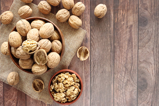 Stock photo showing close-up, elevated view of some walnuts that are piled high in a brown dish, against a woodgrain background. Raw walnuts are considered to be a very healthy snack food, containing a wealth of essential Omega-3 fatty acids, antioxidants and protein, and boasting a list of health benefits while reducing stress.