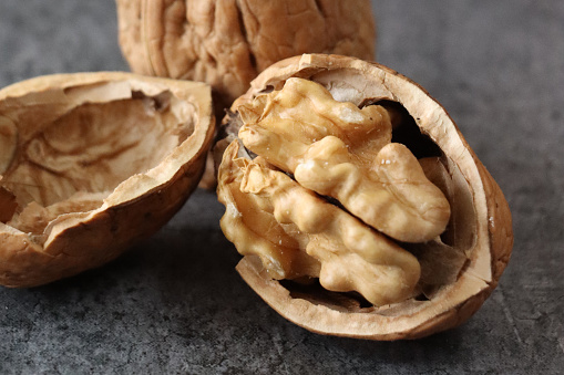 Stock photo showing close-up, elevated view of some shelled and unshelled walnuts against a mottled grey background. Raw walnuts are considered to be a very healthy snack food, containing a wealth of essential Omega-3 fatty acids, antioxidants and protein, and boasting a list of health benefits while reducing stress.