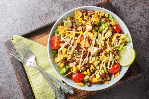 Easy taco salad is made with seasoned ground beef, crisp lettuce, vegetables, cheese and flavorful toppings closeup on the plate on the table. Horizontal top view from above