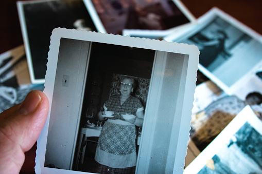 Hand holds vintage photograph of female with pile of old photos in background.  Please view my 