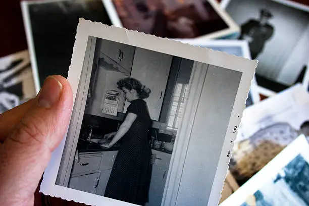 Hand holds vintage photograph of female with pile of old photos in background.  Please view my