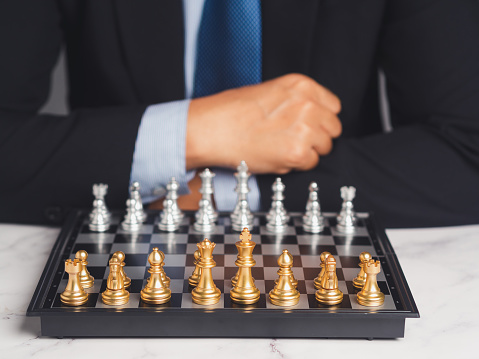 A businessman in a suit playing a game of chess on a chessboard while sitting at the table. Concept of Business Strategy and Planning.