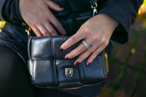 Close-up of a woman opening an unbranded black leather bag while sitting in an autumn park. The girl checks her bag to make sure everything is in place. Attenzione pickpocket