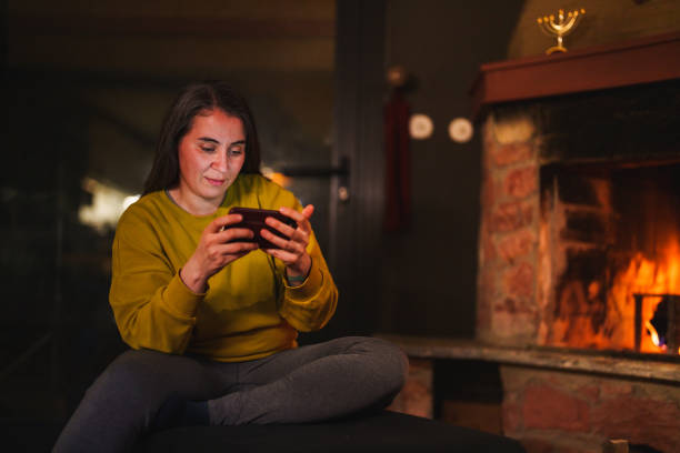 istock Woman using mobile phone in front of a fire place at home 1822176312