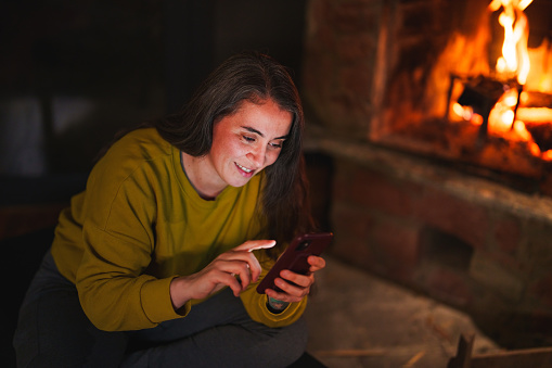 Woman using mobile phone in front of a fire place