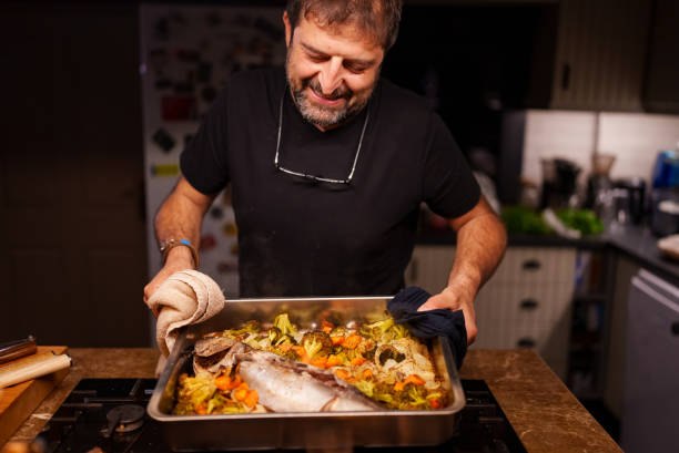 Man holding a hot oven tray with cooked fish stock photo