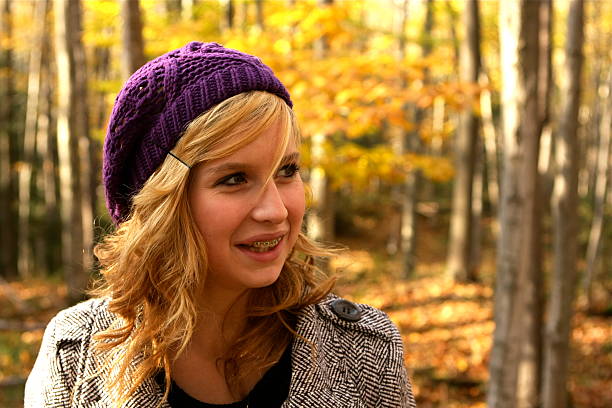 A pretty fifteen year old girl smiles as she stands in the woods in autumn.