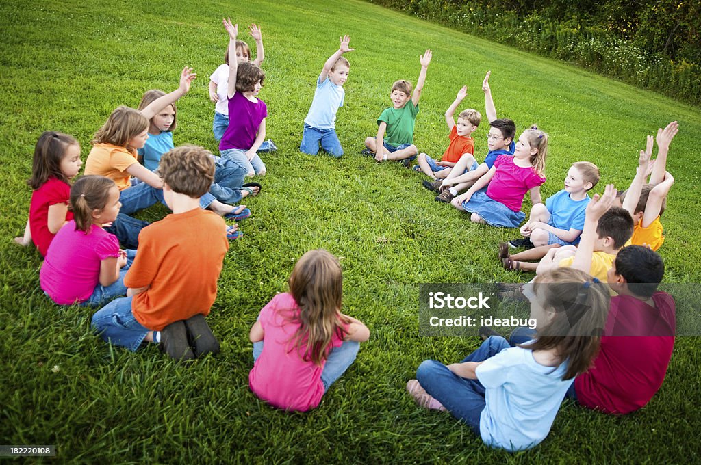Jungen und Mädchen sitzt in einem Kreis Raising Hands - Lizenzfrei Gras Stock-Foto
