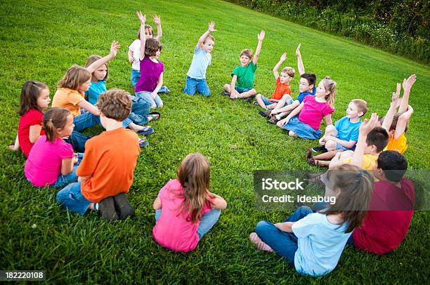 Jungen Und Mädchen Sitzt In Einem Kreis Raising Hands Stockfoto und mehr Bilder von Gras
