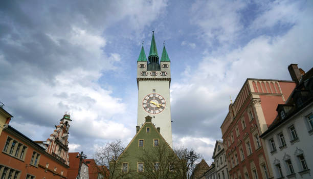 A detailed view of a Gothic clock tower with ornate architectural features, set against a blue sky with the moon visible in the background. The striking contrast of the dark tower and bright sky creates a dramatic and captivating image.