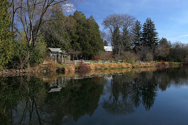 Autumn Scenic Reflection Reflection of autumnal scenic with a blue sky and a mill pond. Wooden shack on the shore. burton sussex stock pictures, royalty-free photos & images