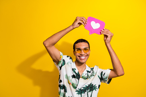 Photo of cheerful cool guy dressed stylish clothes arms above head showing pink paper card isolated on vivid yellow color background.