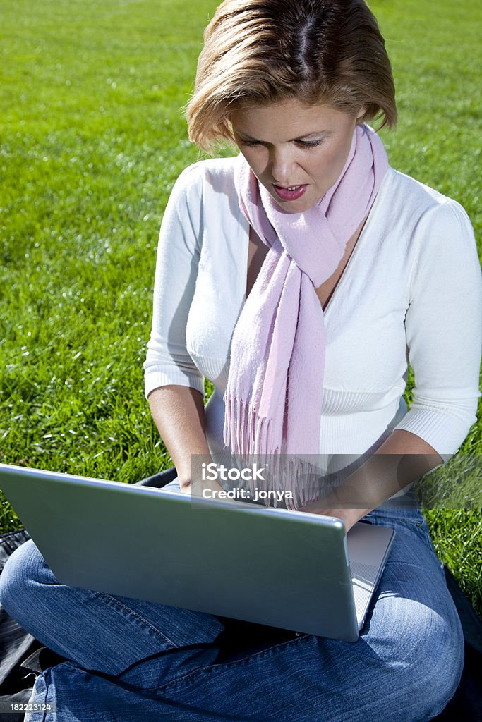 Normali donna seduta Gambe incrociate sull'erba utilizzando il computer portatile - Foto stock royalty-free di Accessibilità