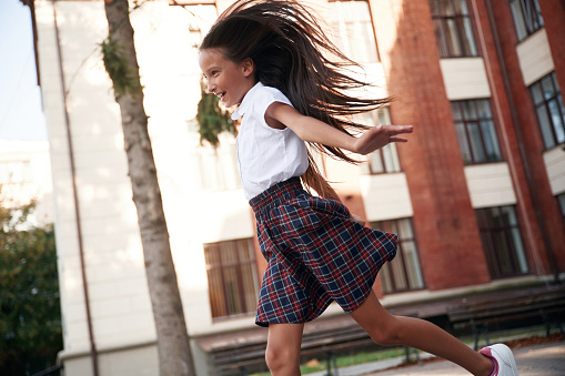 Photo in action, running. School girl in uniform is outdoors near the building.