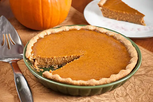 A pumpkin pie with a wedge cut out and sitting on a plate for serving.More homemade pies: