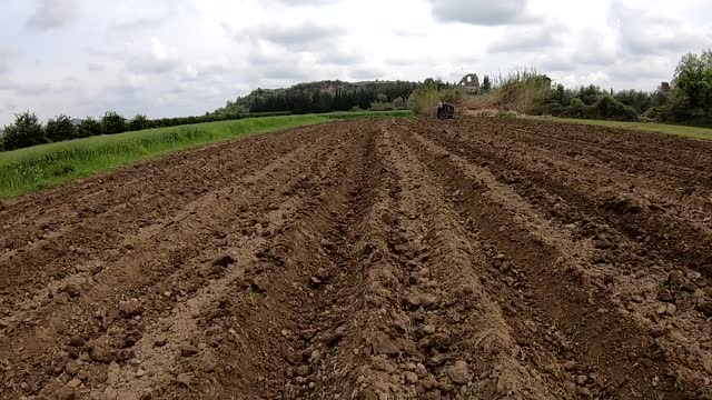 Aerial footage of a drone flying over the field being plowed by a small tractor