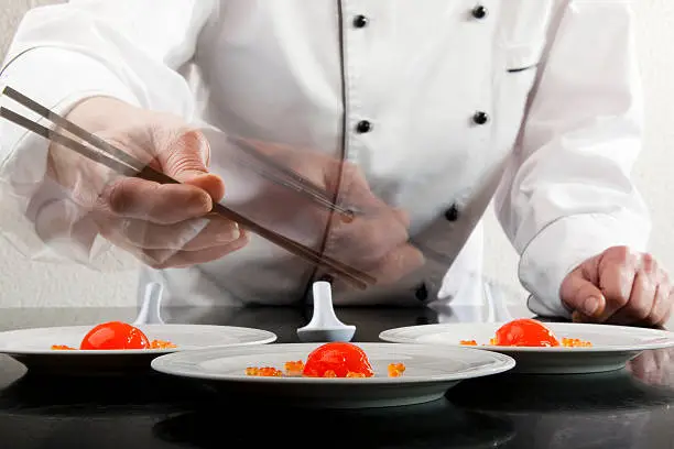 Molecular Gastronomy, Chef cooking up moleculer caviar in a modern kitchen.  Molecular Gastronomy is the hottest new trend in cooking. Chef with three plates of Strawberry Ravioli created using reverse spherification. Close-up shot of Chef placing caviar on plate with chop-sticks.  Motion blur of hands to show action, focus on the foreground plate.