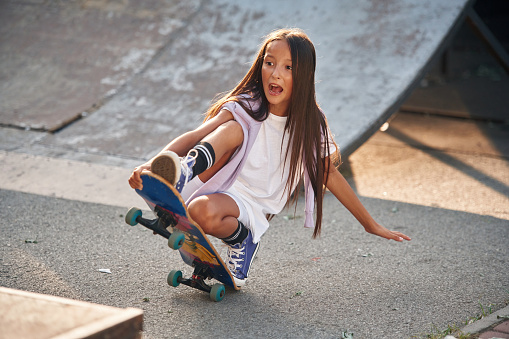 On the ramp. Happy little girl with skateboard outdoors.