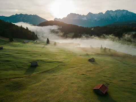 Idyllic view of fog in Bavarian Alps covering the valley, lake and little wooden huts. It's sunrise in autumn