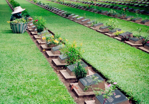 Thai worker gardening graveyard in Kanchanaburi Cemetery