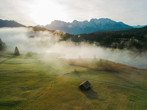 Idyllic view of fog in Bavarian Alps covering the valley, lake and little wooden huts. It's sunrise in autumn