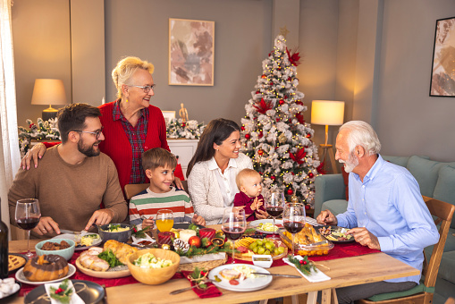 Happy multi-generation family gathered around the table, having Christmas dinner all together at home, speaking to each other and laughing