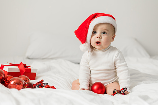 Christmas Baby in Santa Hat, Child holding christmas bauble near Present Gift Box over Holiday Lights background