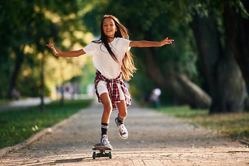 Riding forward. Happy little girl with skateboard outdoors.