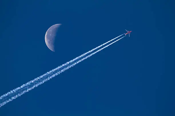 A commercial airplane passing the moon in a clear blue sky.