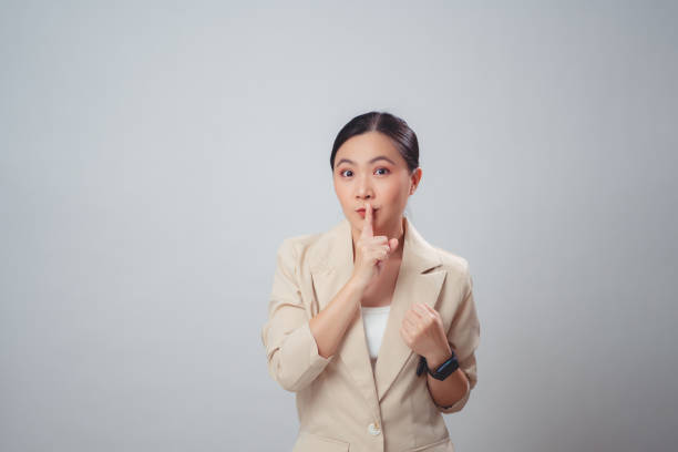 アジアの女性は、唇に人差し指を置いて幸せな笑顔を浮かべ、白い背景に孤立して立っています。 - hand sign stop gesture talking discussion ストックフォトと画像