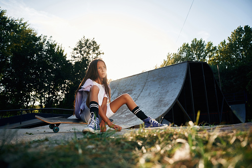 Beautiful summer time in the park, sitting. Happy little girl with skateboard outdoors.