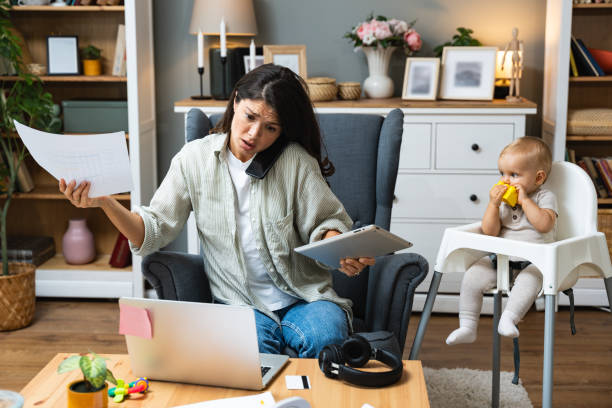 istock Mother working on laptop and talking on computer webcam video call communication with business partners while baby playing. Woman work from home and caring for kids. 1822270338